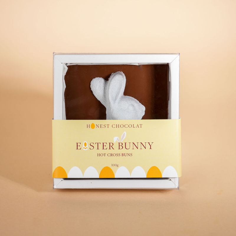 Hot cross bun shaped like an Easter bunny in a box with 'Honest Chocolat' branding on a beige background.