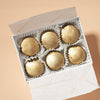 A box of six salted caramel chocolate bonbons in a box, set on a beige background.