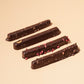 Four chocolate-covered caramel bars arranged in a row on a plain beige background.