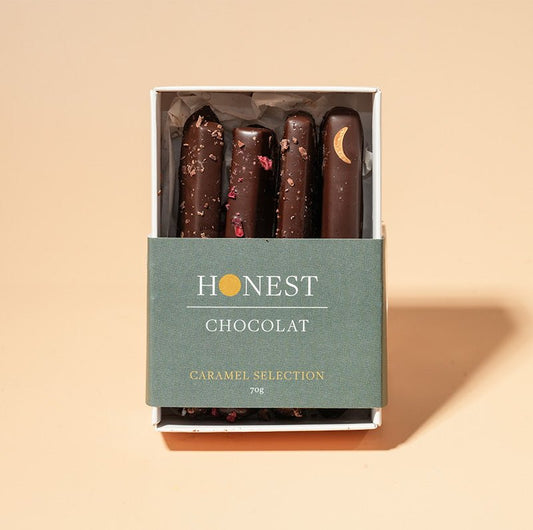 A gift box of dairy-free caramel selection, with varieties including raspberry & pink peppercorn, salted, and dark chocolate passion fruit and kawakawa. The box is labeled 'HONEST CHOCOLAT' and the caramels are visible through a clear window.