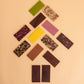 Rectangular chocolate bars in assorted colors and toppings are arranged in a Christmas tree-like pattern on a solid beige background.