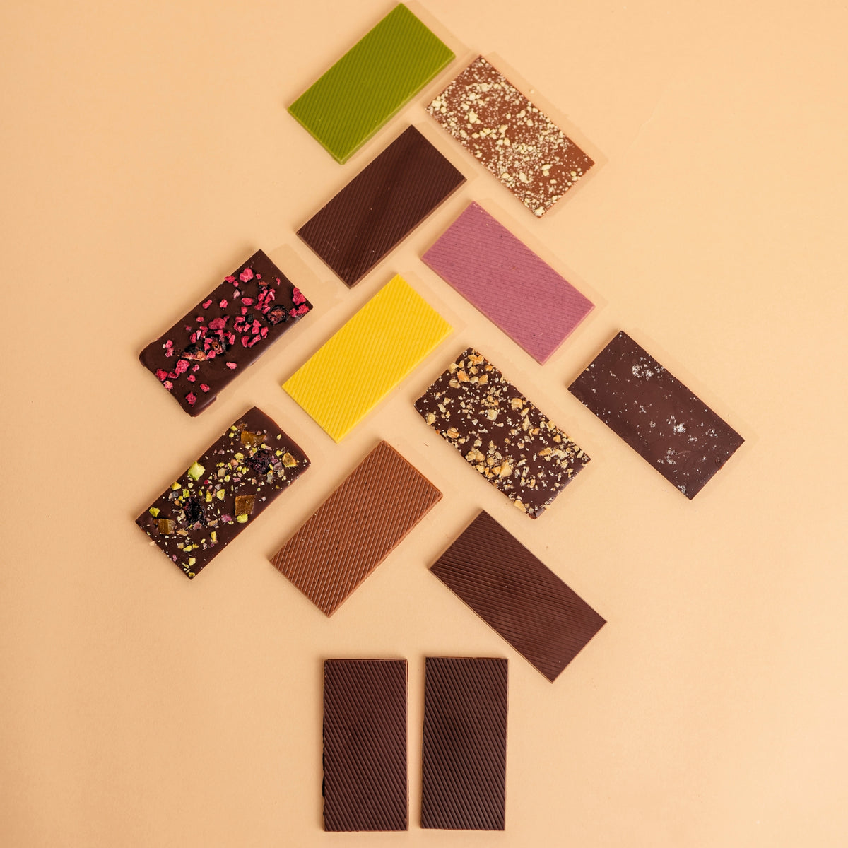 Rectangular chocolate bars in assorted colors and toppings are arranged in a Christmas tree-like pattern on a solid beige background.