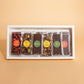 A white rectangular gift box containing individually wrapped chocolate bars with colorful circular labels, set against a solid peach background.