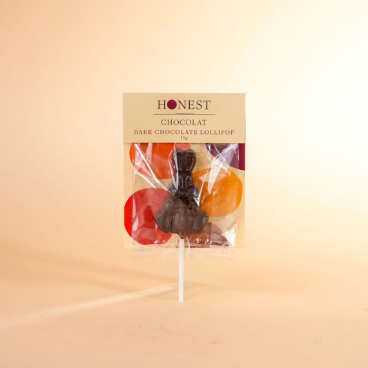 Dark chocolate lollipop in a clear package with 'Honest Chocolat' branding on a beige background.