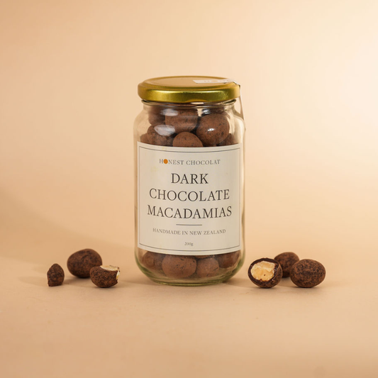 Jar of dark chocolate macadamias with an off-white label on a warm beige background
