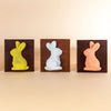 Three chocolate bunny molds in yellow, white, and orange on a beige background