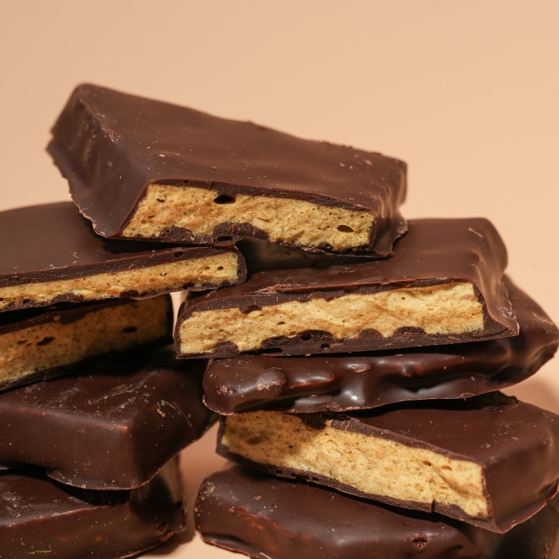 A close-up view of a stack of thick chocolate-covered hokey pokey, set against a warm beige background