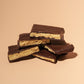 A close-up view of a stack of thick chocolate-covered hokey pokey, set against a warm beige background