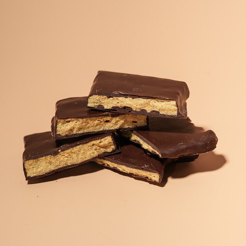 A close-up view of a stack of thick chocolate-covered hokey pokey, set against a warm beige background