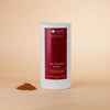 Honest Chocolat hot chocolate powder canister with a small pile of powder on a beige background