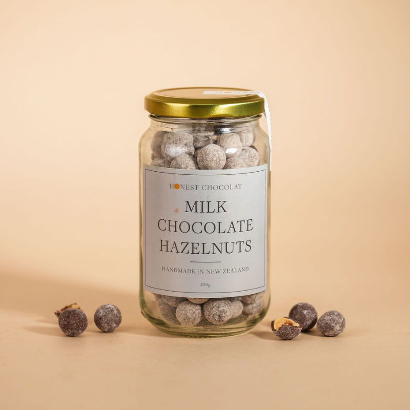 Jar of milk chocolate hazelnuts with a gold lid on a beige background