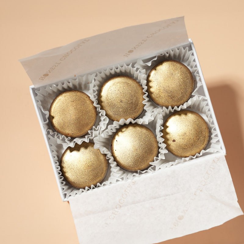 A box of six salted caramel chocolate bonbons in a box, set on a beige background.