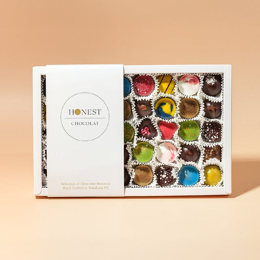 A box of assorted chocolate bonbons from Honest Chocolat, with each bonbon uniquely shaped and colored, displayed in a well-packaged and arranged box