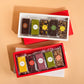 Two red gift boxes of assorted gourmet chocolate bars arranged on a warm beige background for an advent calendar. The top box is open and shows four dark chocolate bars with different flavours like Matcha, Peppermint, and Mango.