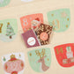 An embroidered Christmas advent calendar fabric panel with numbered sections and festive illustrations, showing two packaged treats placed in the center compartments. The flavours for the chocolate bars are Mixed Berry and Tea and Biscuit.