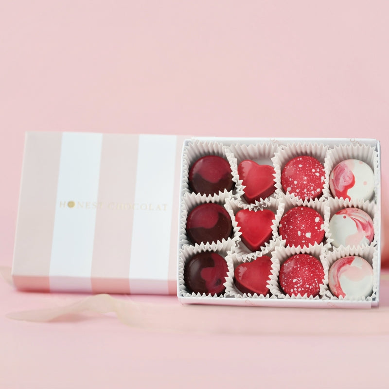 Box of assorted red and white bonbon chocolates on a pink background